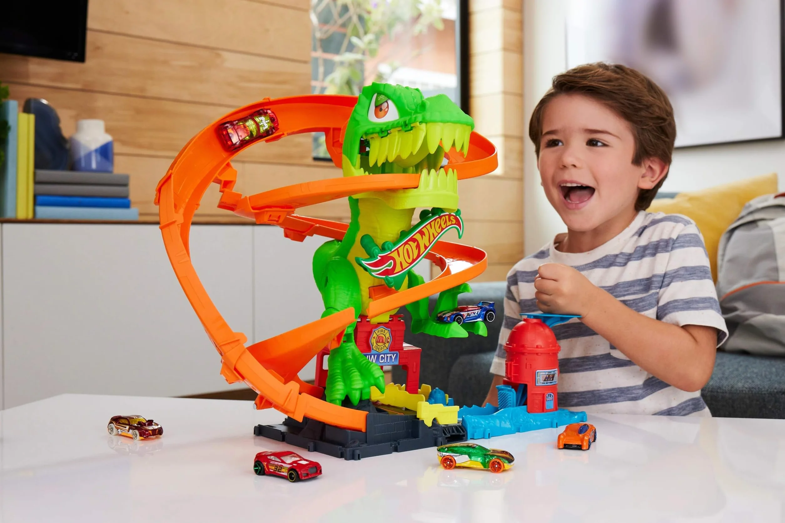 Hot Wheels City - T-Rex Battaglia Infuocata, playset stazione dei pompieri con dinosauro occhi rotanti e pista per gareggiare, camion dei pompieri incluso, giocattolo per bambini, 4+ anni, JBM73